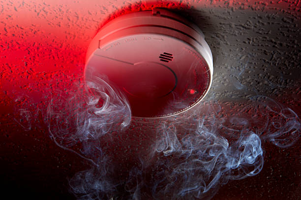 Close up shot of ceiling mounted smoke detector with white smoke and red warning light